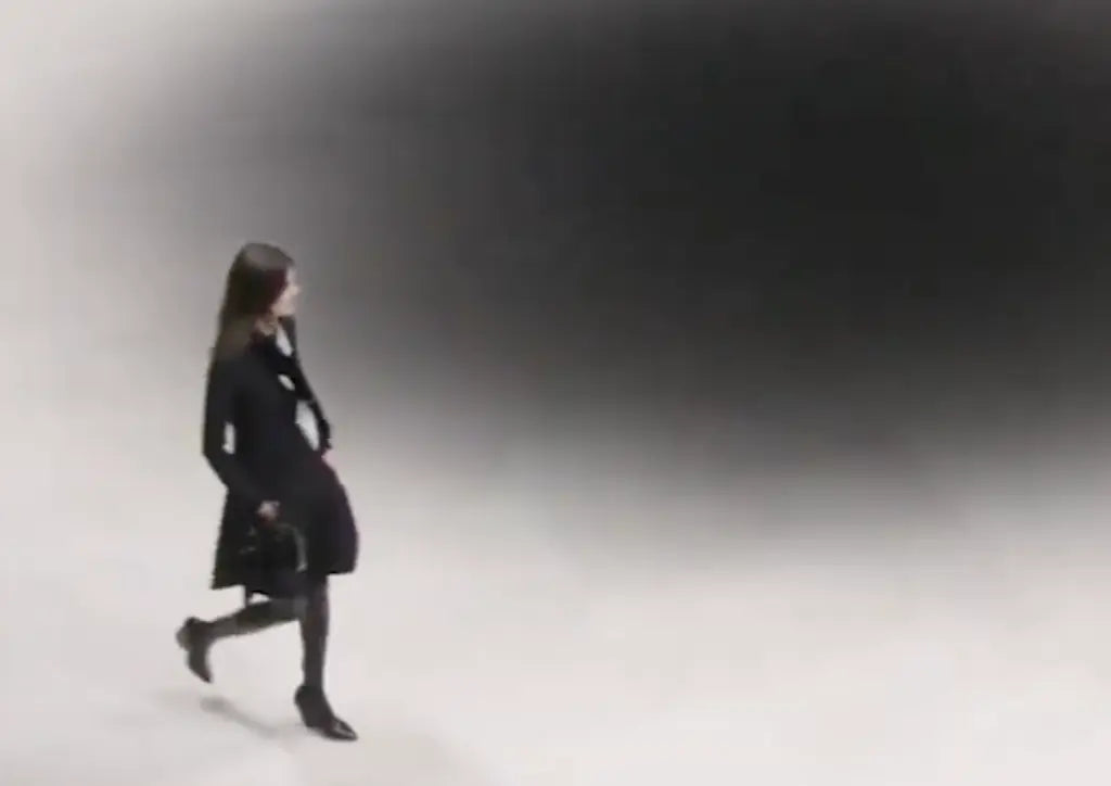 Model in the runway wearing long-sleeve black midi dress with thigh-high boots and a black and white scarf tied around her neck